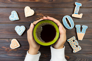 Female hands with coffee and heart shaped cookies on wooden table, top view. Love concept