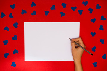 Woman's hand write on white blank papert above red background with many blue hearts around. Love concept