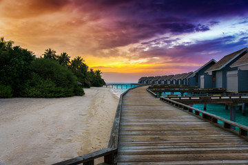 Farbenfroher Sonnenuntergang hinter einem Holzsteg und Bungalows auf dem Wasser auf den Malediven
