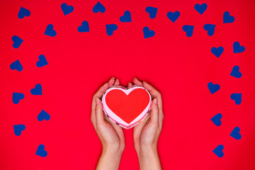 Woman's hands hold red heart on red background with many blue hearts around. Love card