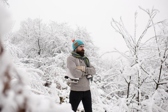 Bearded man with skates in snowy forest.
