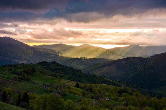 gorgeous mountainous countryside at sunset. beams of light break through heavy clouds. rolling hills with rural fields in the shade. spectacular springtime landscape