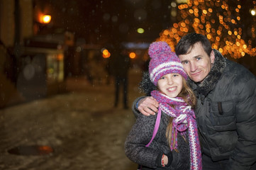 Father and daughter are walking at the night city during snowfall