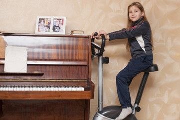 The young girl in a sports suit is riding a stationary bike at home