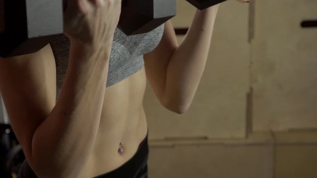 Fitness lady doing biceps dumbbell curls in gym. Woman holds free weight, begins to bend arms, lifting tools up, after reaching top point, returns to starting position slowly