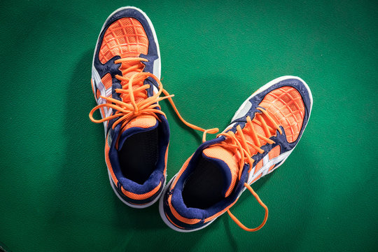 Top down view of orange and white badminton sport shoes on the green floor
