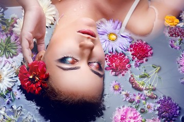 Brunette girl with glamorous makeup and clean the skin in water with flowers close-up top view