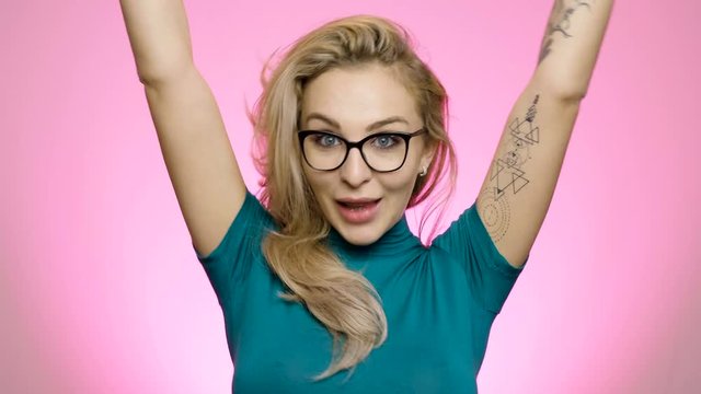 Pretty young woman making silly faces at camera on vivid pink background in studio