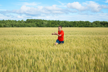 Boy, a teenager runs across the field with ears of wheat grains