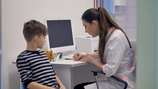 Friendly doctor writes prescription for young boy.