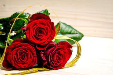 Red roses are shrouded in a golden ribbon, which has a heart shape.