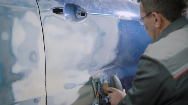 close shot at the man's hands, who level the dent on the car door in order to rectify the damage after the accident