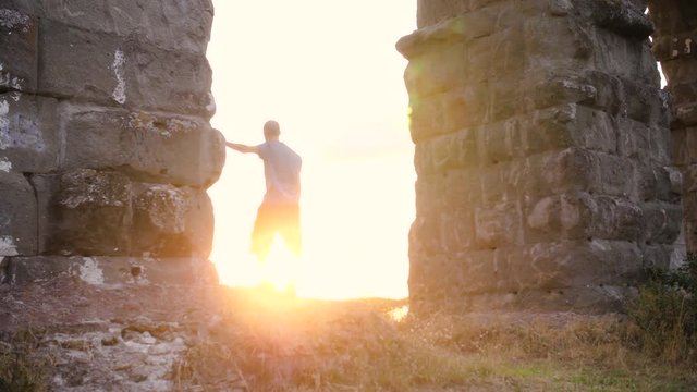 Young man in sportswear stretching under ancient roman aqueduct Appio Claudio arch. Excercising outdoor in peaceful park in Rome at sunset slow motion.