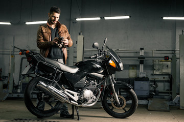 Naklejka premium Młody człowiek stoi blisko motocyklu w garażu w skórzanej kurtce