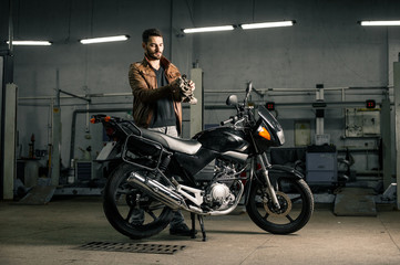 Fototapeta na wymiar Young man in leather jacket standing near motorcycle in garage