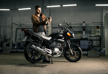 Fototapeta na wymiar Young man in leather jacket standing near motorcycle in garage