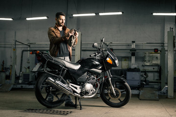 Plakat Young man in leather jacket standing near motorcycle in garage
