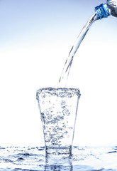 Pouring water and splashing in the glass with reflection on mirror.