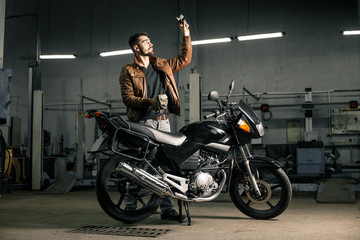 Fototapeta na wymiar Young man in brown leather jacket standing near motorcycle in garage