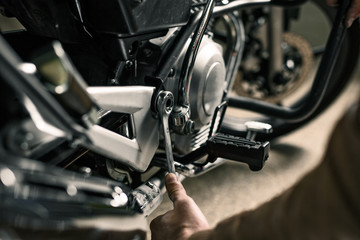 Biker's hands holding wrench near motorcycle