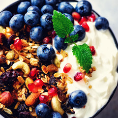 Tasty homemade granola, yogurt, fresh organic berries, pomegranate, mint on grey concrete background with copy space, top view. Square crop
