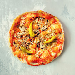 Fresh italian pizza with mushrooms, ham, tomatoes, cheese, olive, pepper on grey concrete background. Copy space. Top view. Square crop