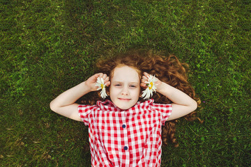 Child with daisy on green grass in a summer park.