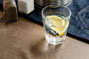 Lemon in glass on the dining table, blue apron, cutlery, iron pot, salt. vegetables food, home cooking concept