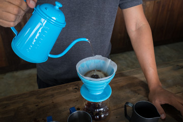 coffee drip in coffee pot pouring into the ceramic cup on the wooden table in coffee shop