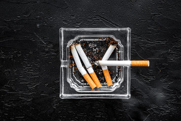 Smoking. Half-smoked cigarettes in ashtray on black background top view