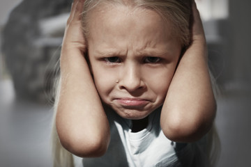 Helpless little girl covering her ears indoors. Child abuse concept