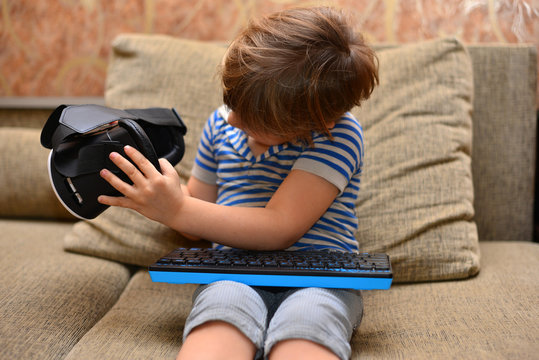 Low angle portrait of little boy wearing VR glasses watching 360 videos and playing augmented reality games at home sitting cross legged on cozy sofa, copy space
