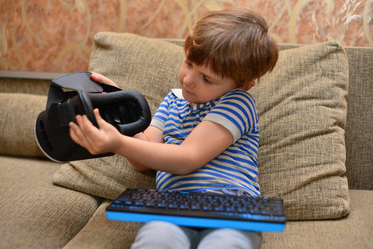 Low angle portrait of little boy wearing VR glasses watching 360 videos and playing augmented reality games at home sitting cross legged on cozy sofa, copy space