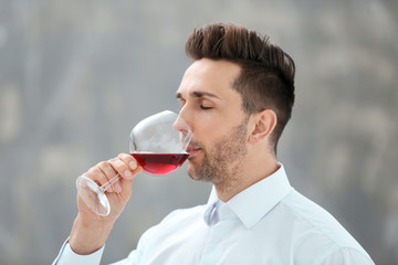 Handsome young man drinking red wine indoors