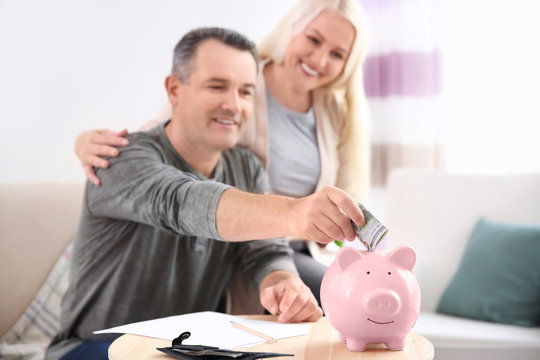 Mature couple putting money into piggy bank at home