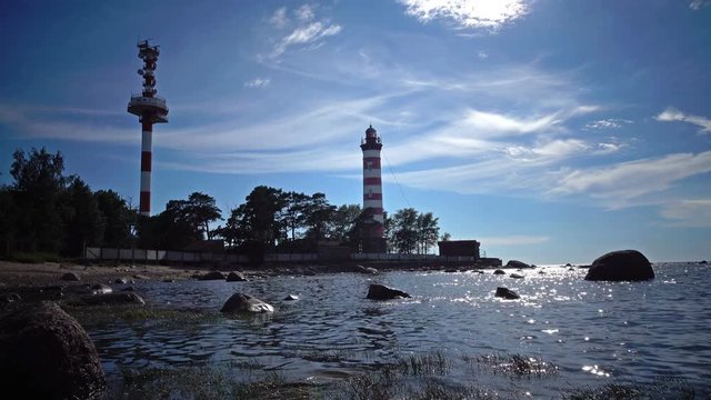 The building of the old beacon on the seashore against the background of the sky with brightly consecrating sun.Sunshine over a Lighthouse. St. Petersburg. Gulf of Finland