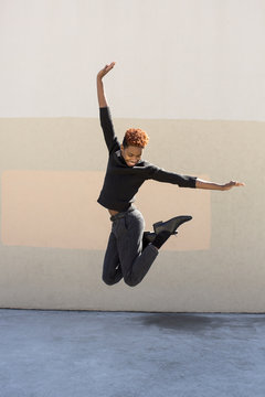 Young black man jumping in a black turtleneck.