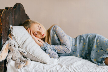 Young beautiful blonde teen sleeping on vintage wooden bed. Cute lovely girl resting on old french...