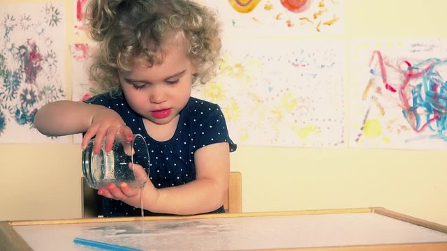 Curious toddler child pour water on table. Excited wet kid playing with water