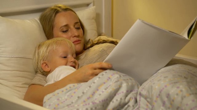 mother and baby son reading a book in bed