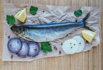 Appetizing salted herring fillet with onion, lemon and spices on parchment.
