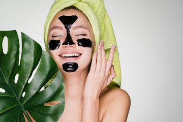young happy girl with a towel on her head applied a black mask to cleanse the skin