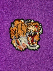 Fototapete Violett Ein Vintage-Tiger-Patch auf einem glitzernden, ultravioletten Hintergrund