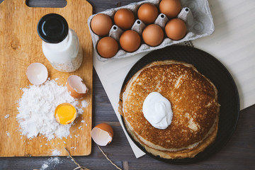 fresh, hot pancakes in a frying pan, eggs, milk, flour on a wooden table. Top view