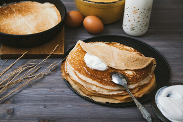 Pancakes in a skillet and ingredients for them on a wooden table