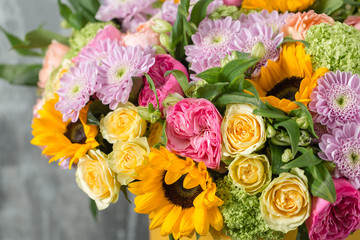 Obraz premium beautiful bouquet of mixed flowers in a vase on wooden table. the work of the florist at a flower shop. a bright mix of sunflowers, chrysanthemums and roses