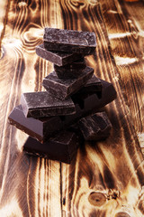 Dark brown chocolate pieces, stacks culinary wooden background.