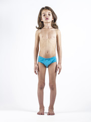 Cute boy in swimming trunks doing gymnastic exercises. White background.