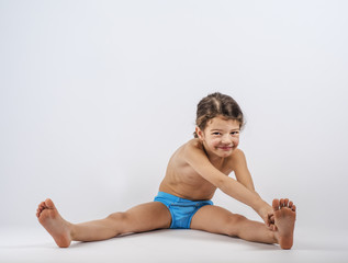 Cute boy in swimming trunks doing gymnastic exercises. Gray background.