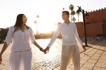 Dreamy couple dressed in white closes walks around African city Marrakesh in a sunny evening
